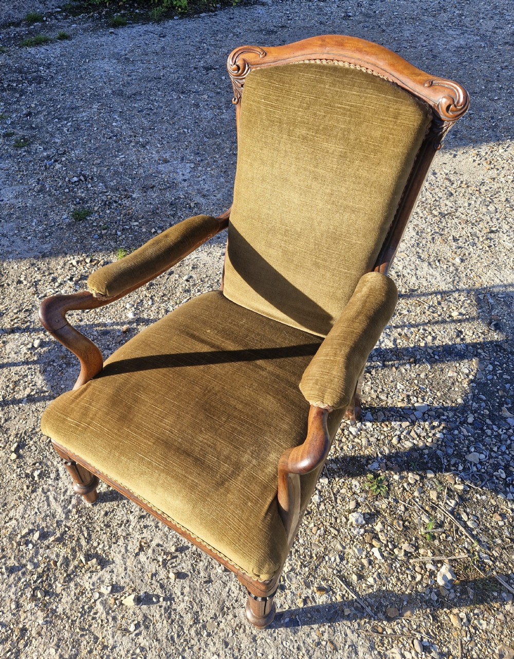 An Early Victorian rosewood armchair featuring olive green velvet upholstery, carved cresting rail, padded armrests, and turned front legs. View IV
