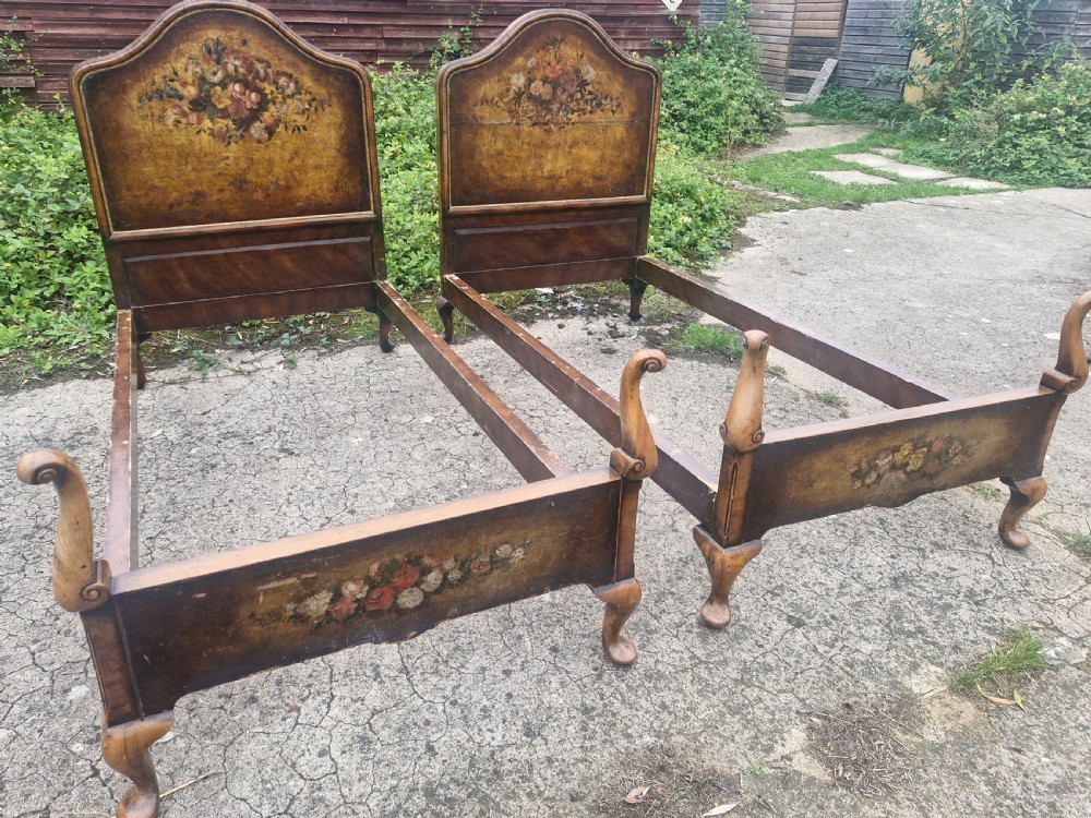 A pair of antique walnut single bed frames featuring arched headboards with floral painted leather panels and scrolled footboard posts. View X