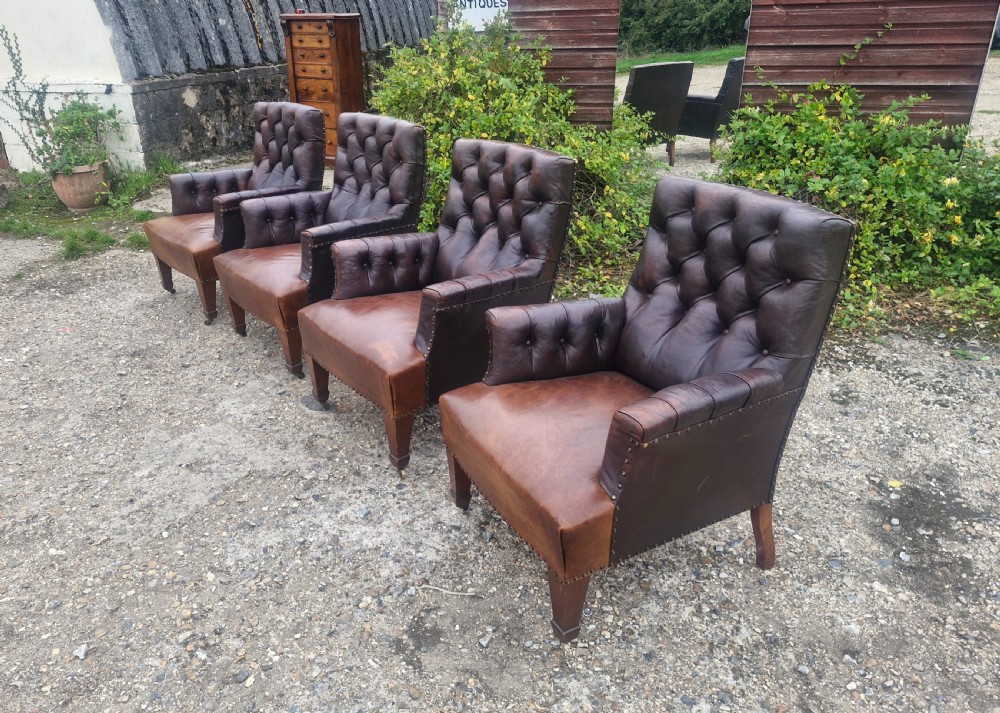 Set of four dark brown leather armchairs featuring deep button tufting, brass studding, and square tapered legs with castors. View II