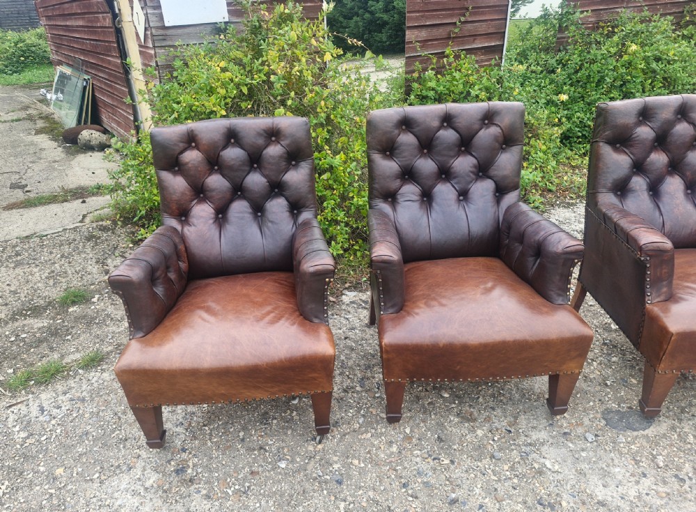 Set of four dark brown leather armchairs featuring deep button tufting, brass studding, and square tapered legs with castors. View III
