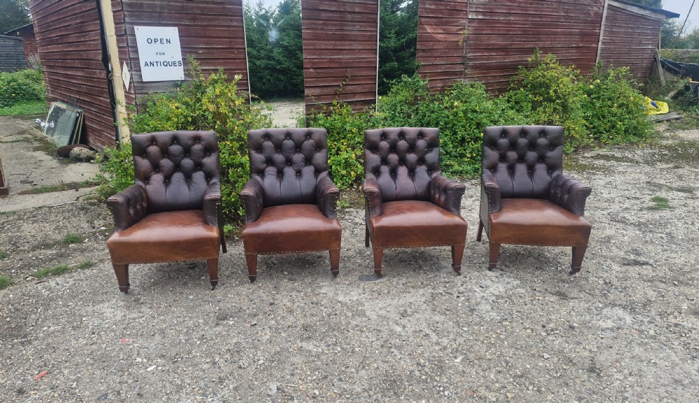 Set of four dark brown leather armchairs featuring deep button tufting, brass studding, and square tapered legs with castors. View V