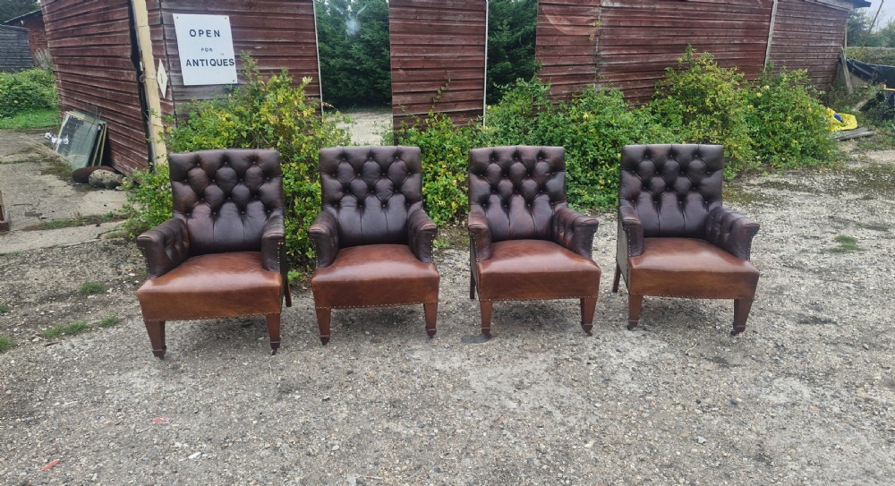 Set of four dark brown leather armchairs featuring deep button tufting, brass studding, and square tapered legs with castors. View VI