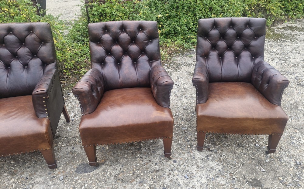 Set of four dark brown leather armchairs featuring deep button tufting, brass studding, and square tapered legs with castors. View XI