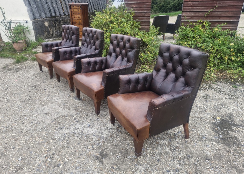 Set of four dark brown leather armchairs featuring deep button tufting, brass studding, and square tapered legs with castors. View XII