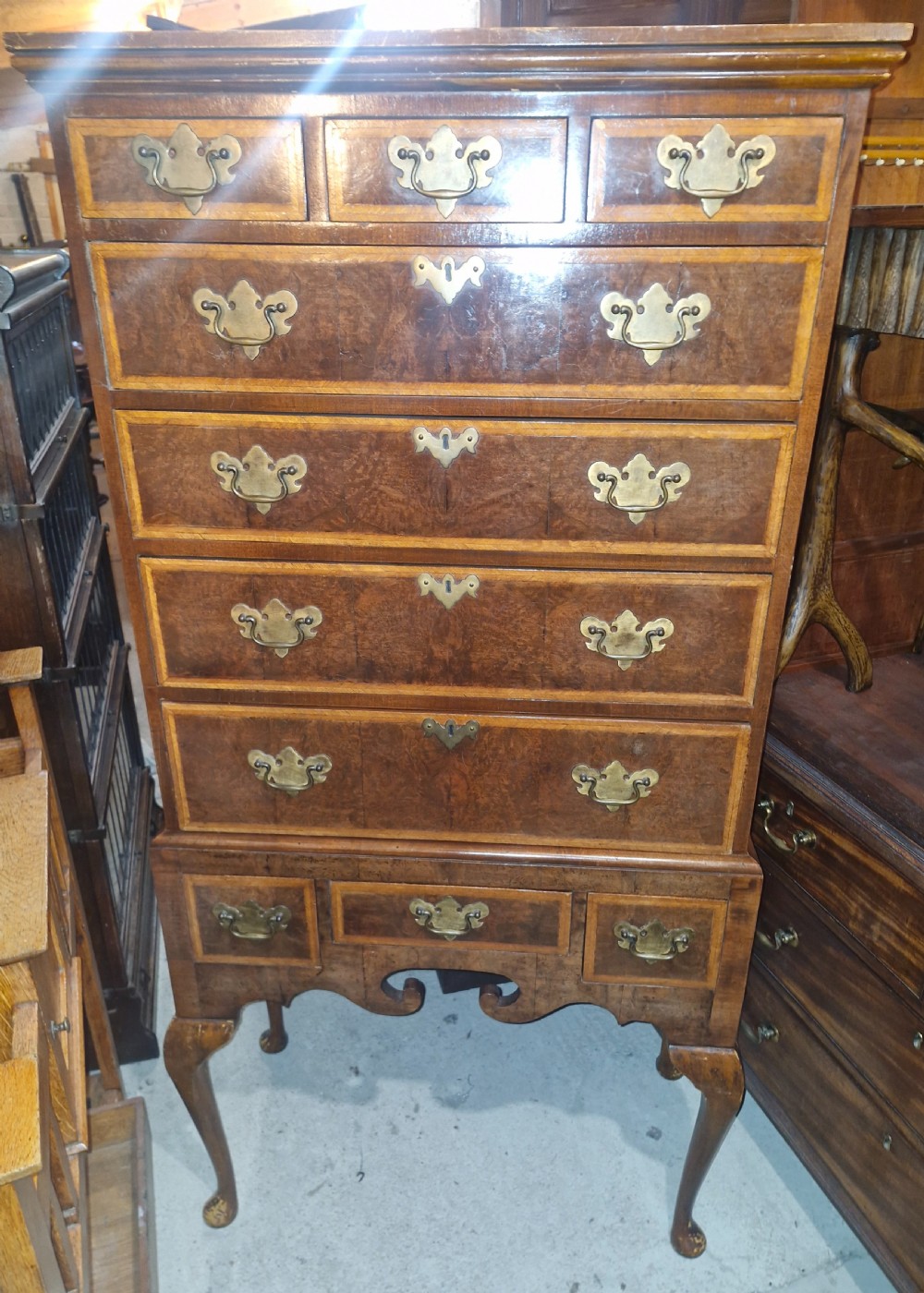 A Queen Anne style burr walnut chest on stand featuring crossbanded drawer fronts, brass drop handles, and a shaped apron raised on cabriole legs.