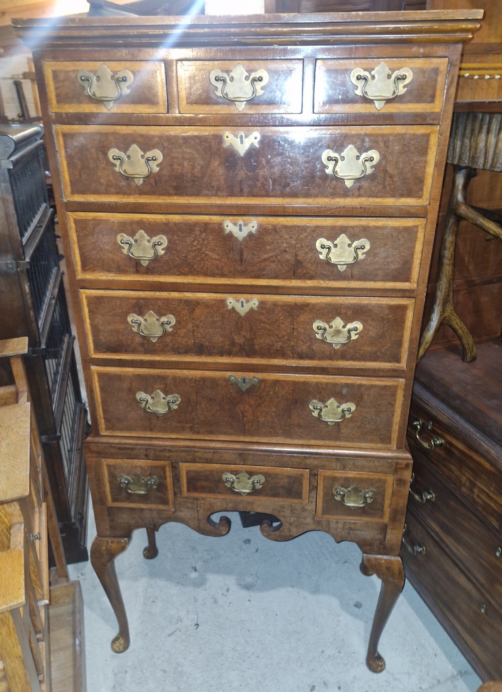 A Queen Anne style burr walnut chest on stand featuring crossbanded drawer fronts, brass drop handles, and a shaped apron raised on cabriole legs. View II