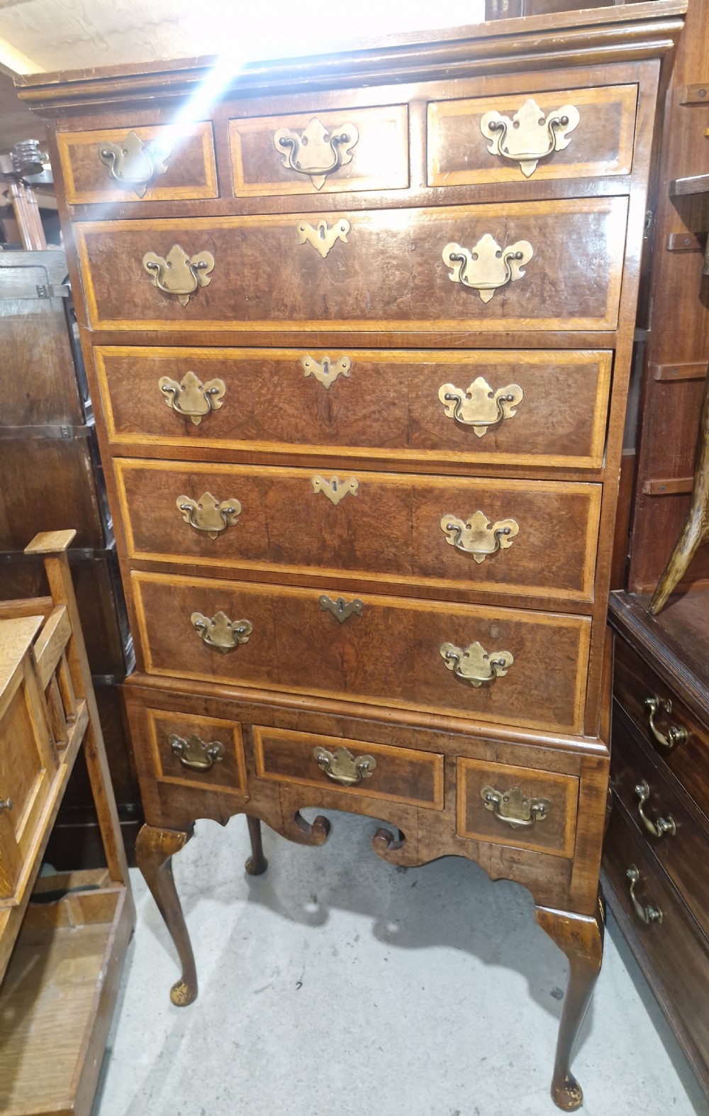 A Queen Anne style burr walnut chest on stand featuring crossbanded drawer fronts, brass drop handles, and a shaped apron raised on cabriole legs. View IV
