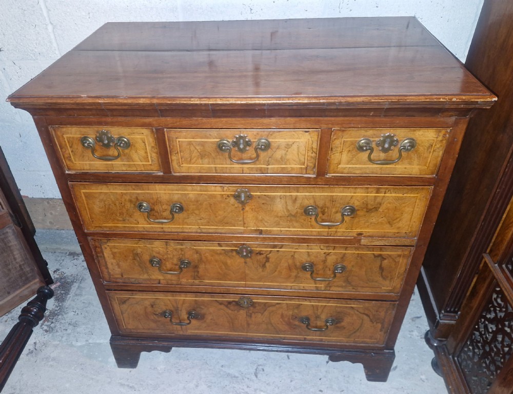 An 18th-century walnut chest of drawers featuring three small top drawers above three long drawers with brass drop handles and bracket feet.