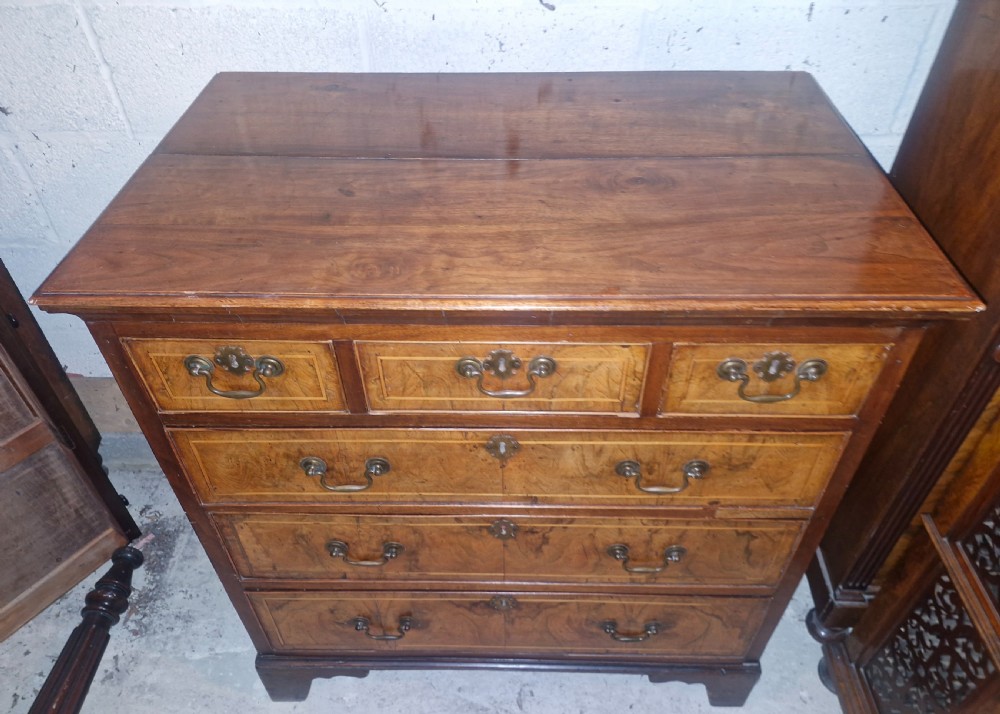 An 18th-century walnut chest of drawers featuring three small top drawers above three long drawers with brass drop handles and bracket feet. View V