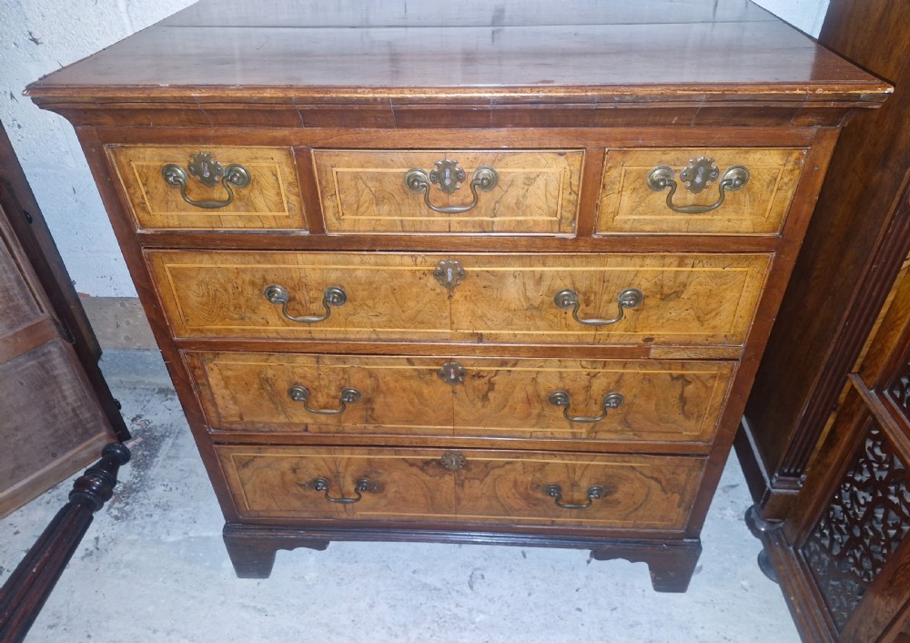 An 18th-century walnut chest of drawers featuring three small top drawers above three long drawers with brass drop handles and bracket feet. View VI