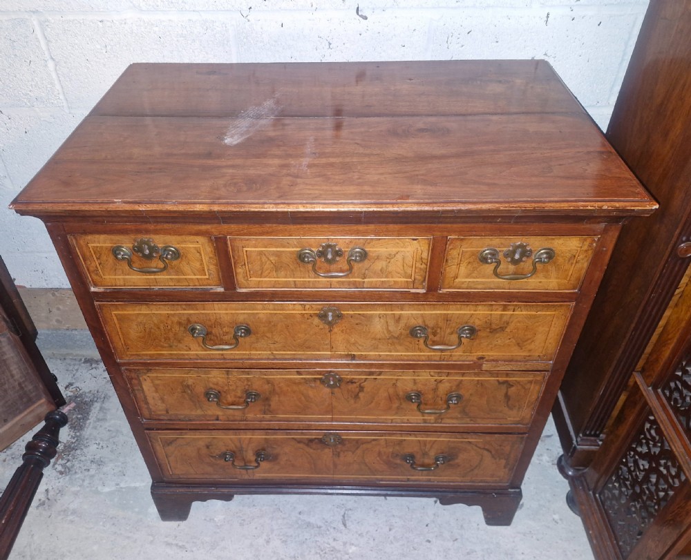 An 18th-century walnut chest of drawers featuring three small top drawers above three long drawers with brass drop handles and bracket feet. View VII