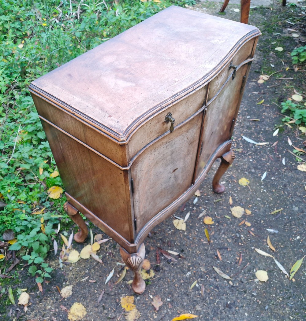 An early 20th-century walnut side cabinet featuring two doors, a serpentine front, drop brass handles, and cabriole legs with shell-carved knees.