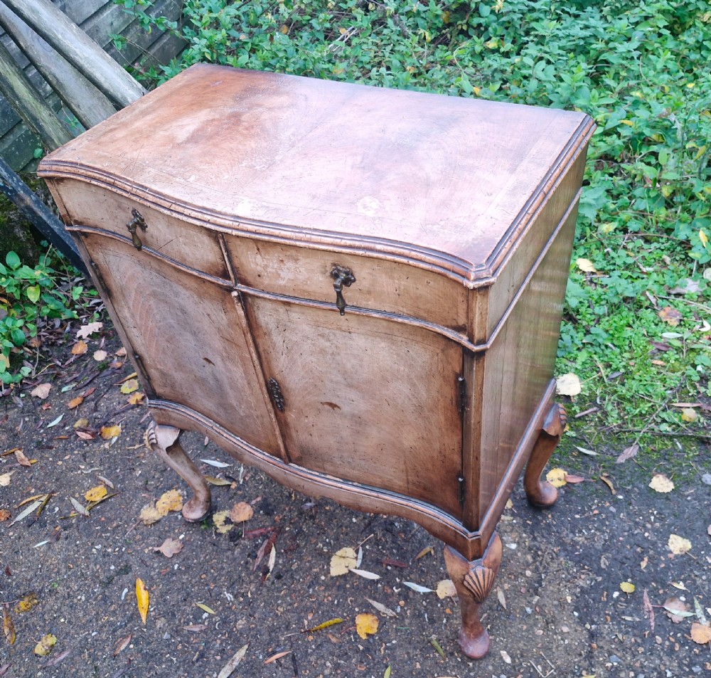 An early 20th-century walnut side cabinet featuring two doors, a serpentine front, drop brass handles, and cabriole legs with shell-carved knees. View III