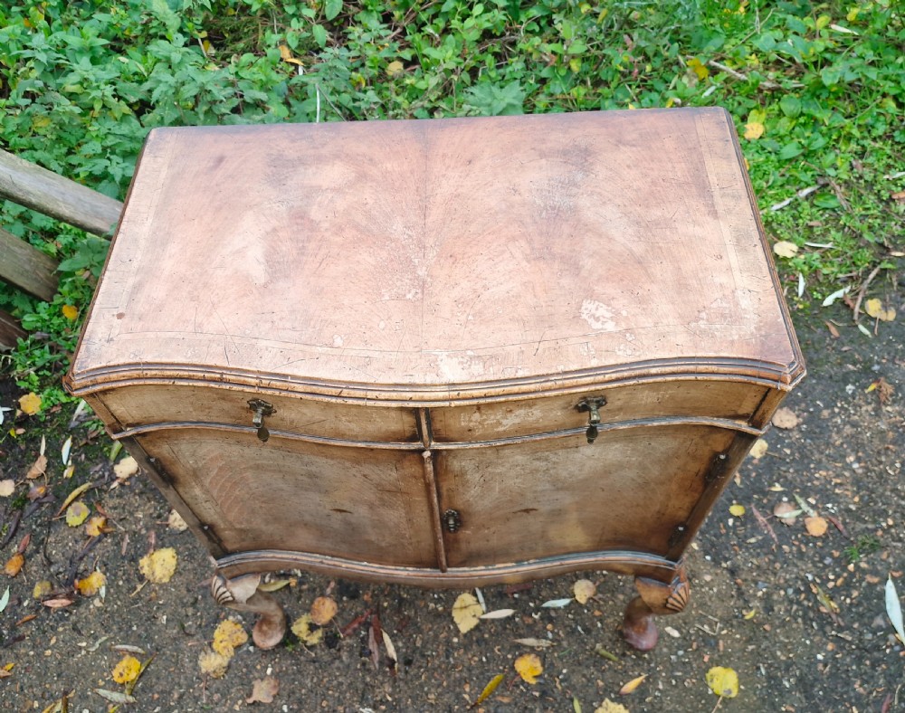 An early 20th-century walnut side cabinet featuring two doors, a serpentine front, drop brass handles, and cabriole legs with shell-carved knees. View V