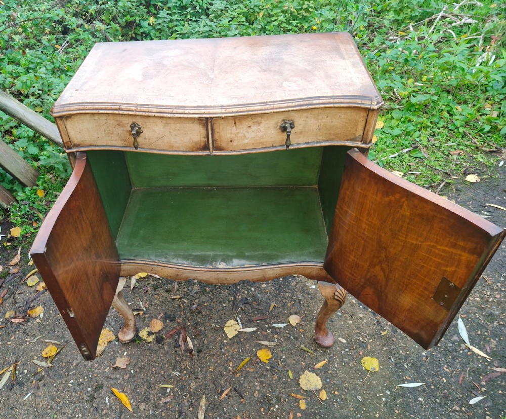 An early 20th-century walnut side cabinet featuring two doors, a serpentine front, drop brass handles, and cabriole legs with shell-carved knees. View VI