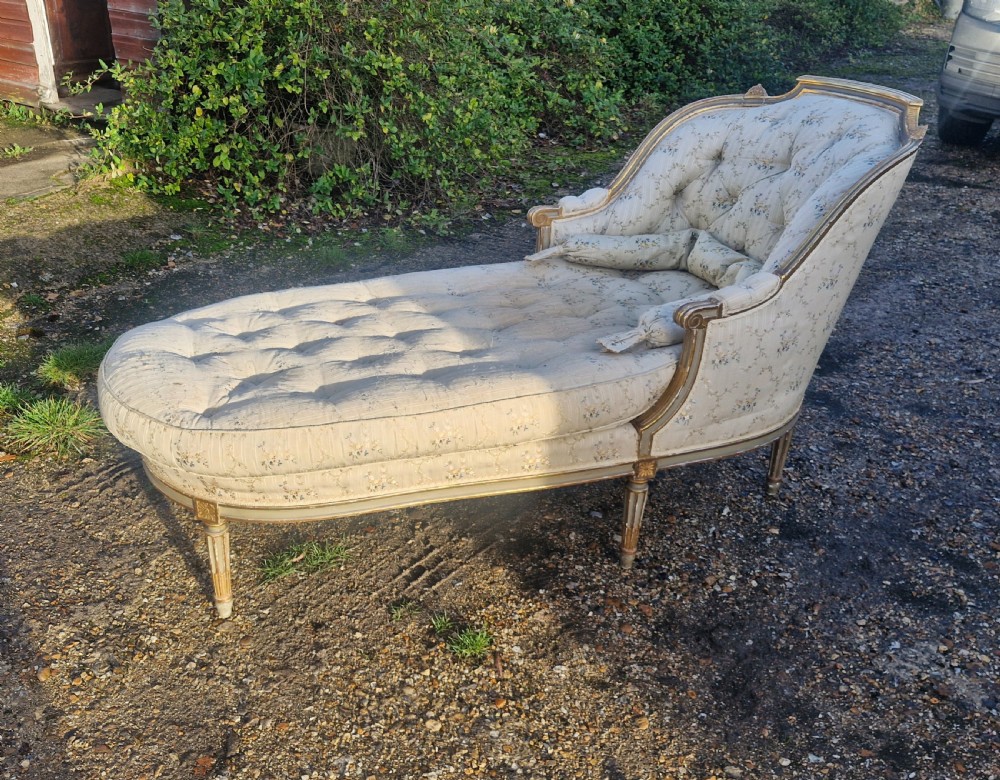 An early 20th-century French style giltwood day bed featuring button-tufted cream floral fabric, fluted tapered legs, and an asymmetrical curved backrest.