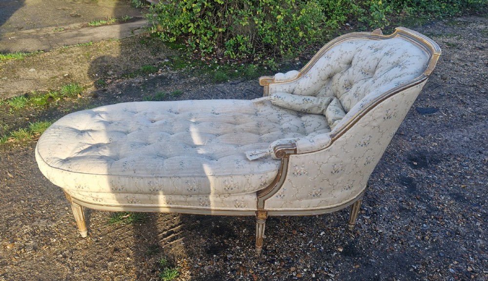 An early 20th-century French style giltwood day bed featuring button-tufted cream floral fabric, fluted tapered legs, and an asymmetrical curved backrest. View IX