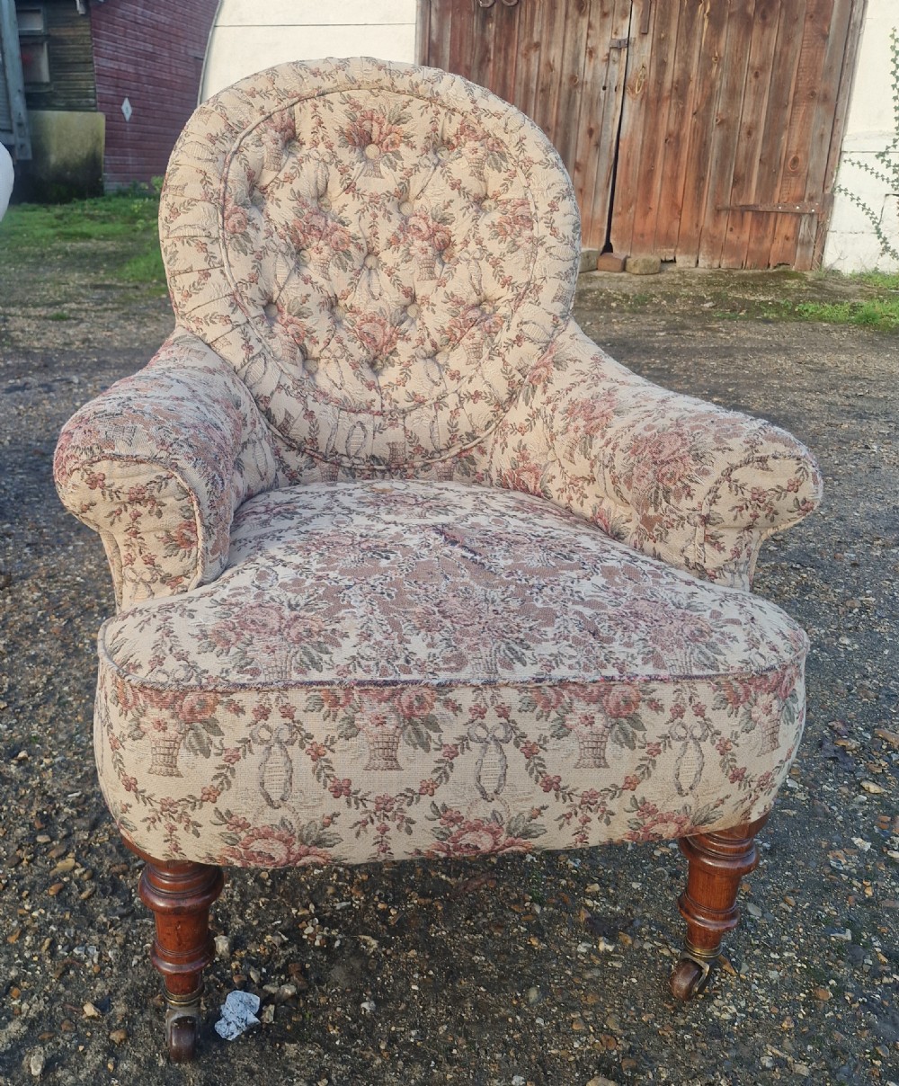 A Victorian armchair featuring floral tapestry upholstery, deep button tufting on the backrest, padded armrests, turned wooden legs, and brass castors. View III