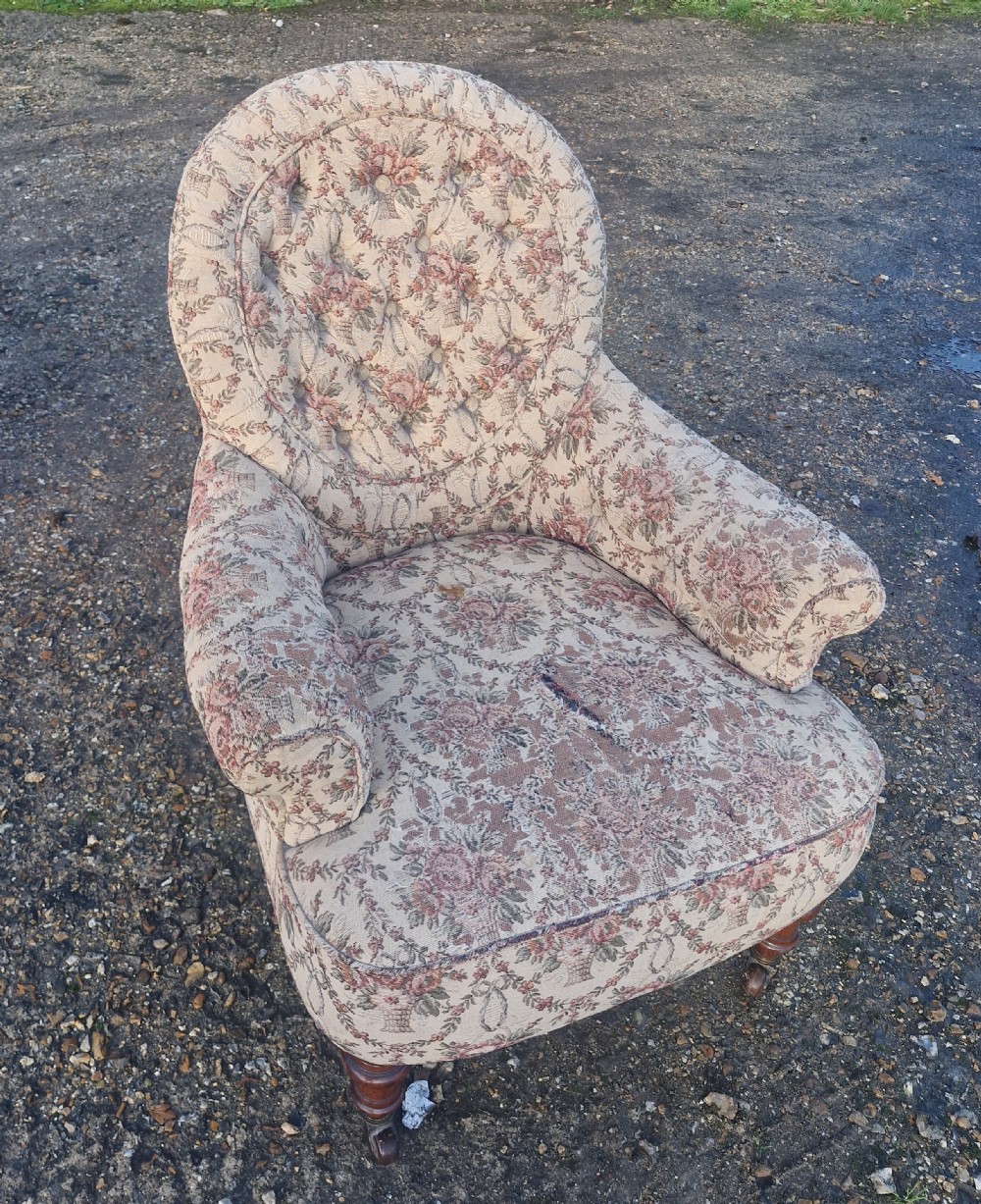 A Victorian armchair featuring floral tapestry upholstery, deep button tufting on the backrest, padded armrests, turned wooden legs, and brass castors. View V