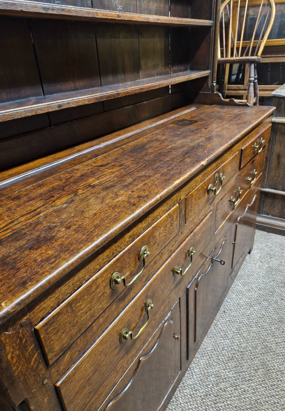 An early nineteenth-century two-part dark oak Welsh dresser featuring a three-shelf plate rack over a sideboard base with drawers and fielded panel cupboard doors. View XI