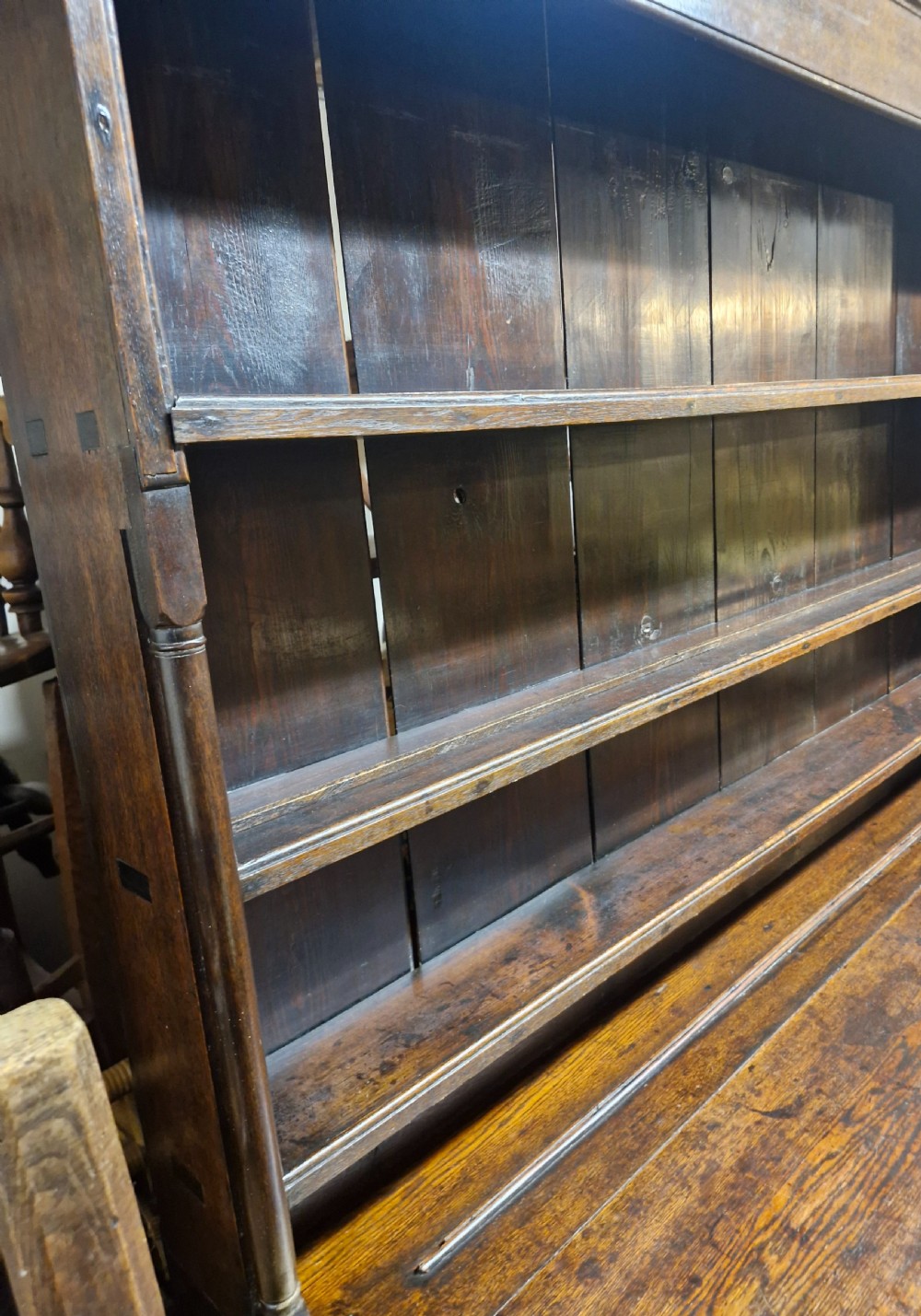 An early nineteenth-century two-part dark oak Welsh dresser featuring a three-shelf plate rack over a sideboard base with drawers and fielded panel cupboard doors. View XII