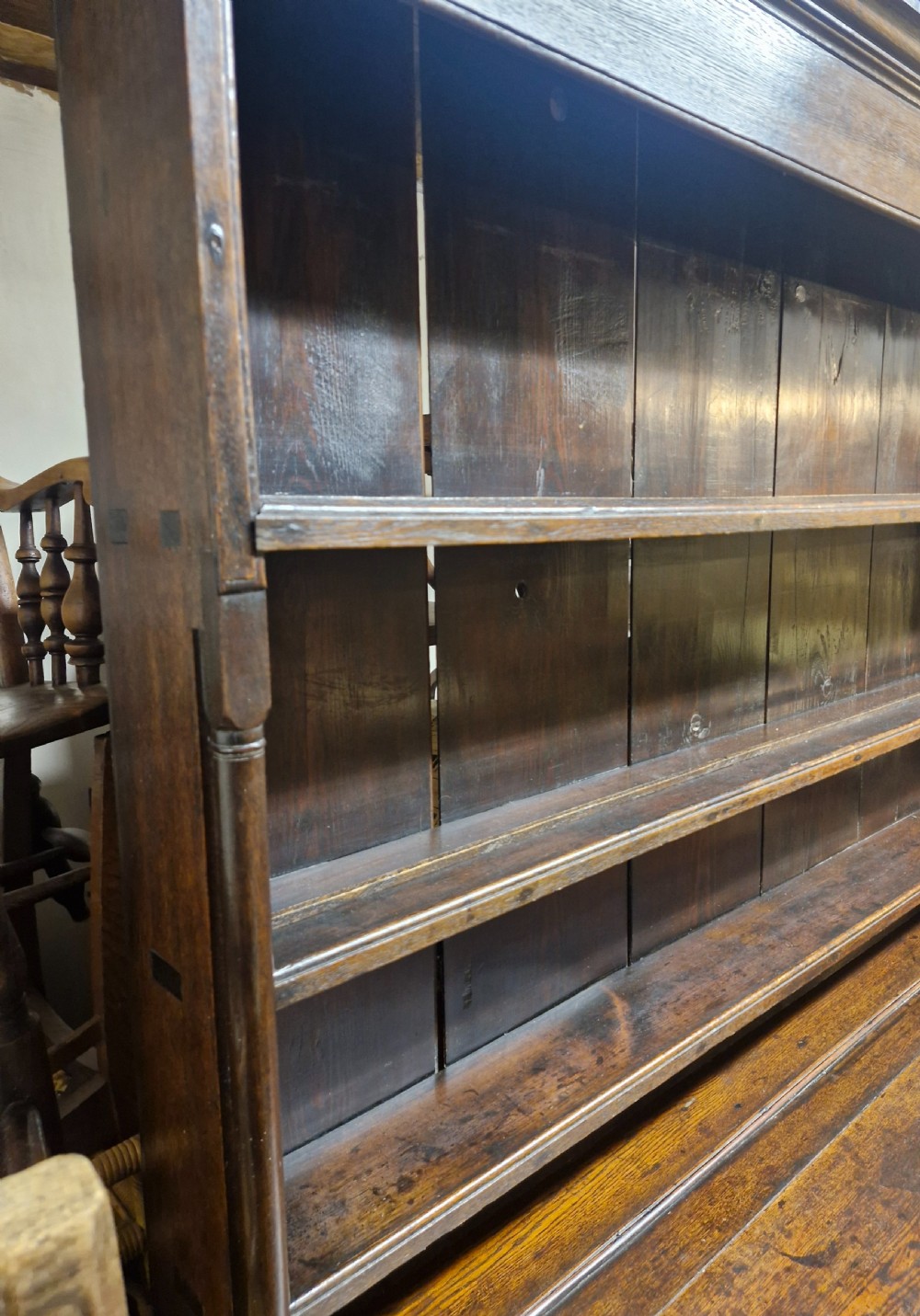 An early nineteenth-century two-part dark oak Welsh dresser featuring a three-shelf plate rack over a sideboard base with drawers and fielded panel cupboard doors. View XIII