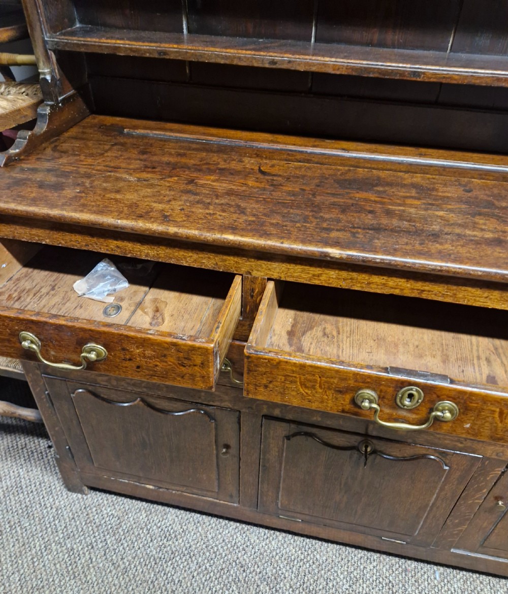 An early nineteenth-century two-part dark oak Welsh dresser featuring a three-shelf plate rack over a sideboard base with drawers and fielded panel cupboard doors. View XV