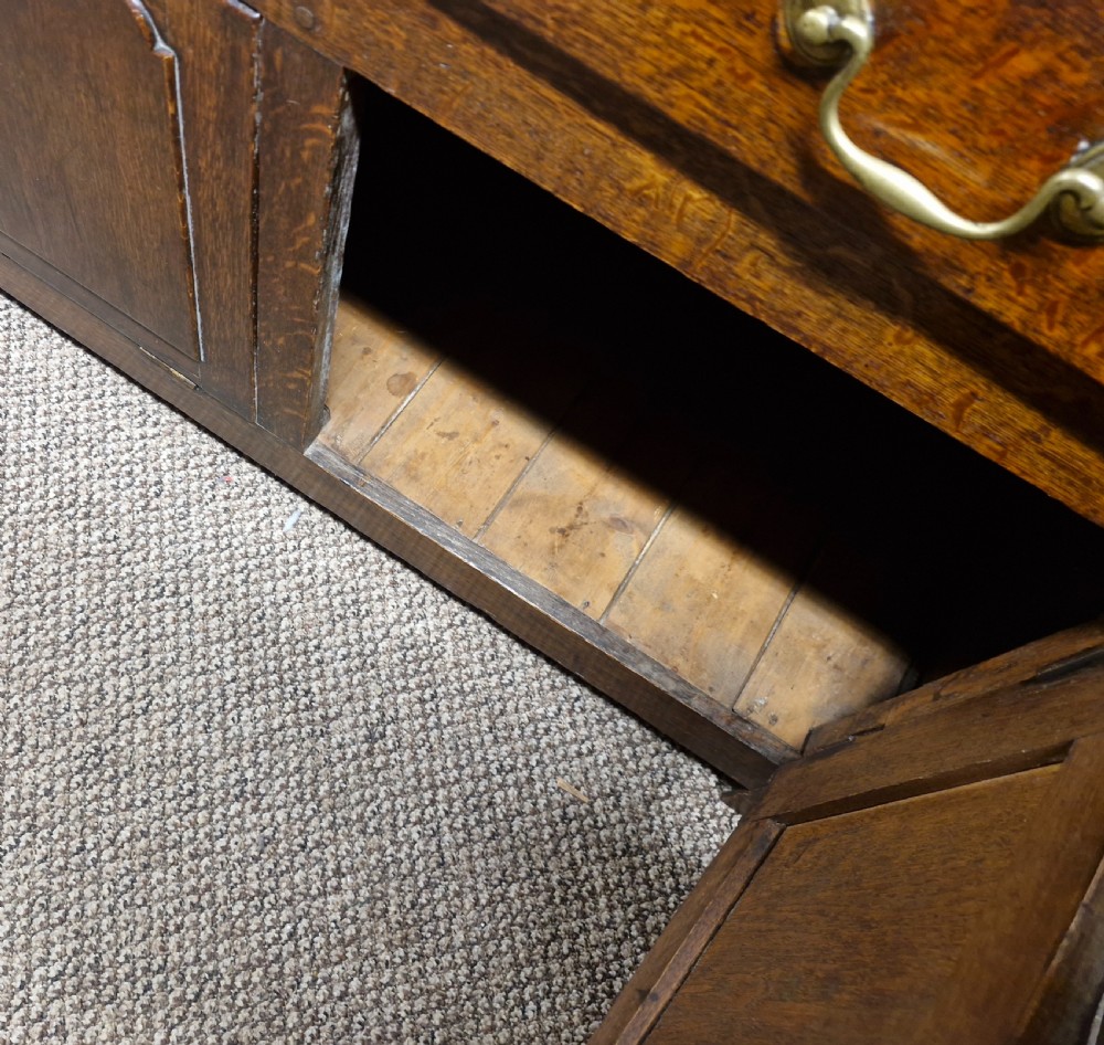 An early nineteenth-century two-part dark oak Welsh dresser featuring a three-shelf plate rack over a sideboard base with drawers and fielded panel cupboard doors. View XVII