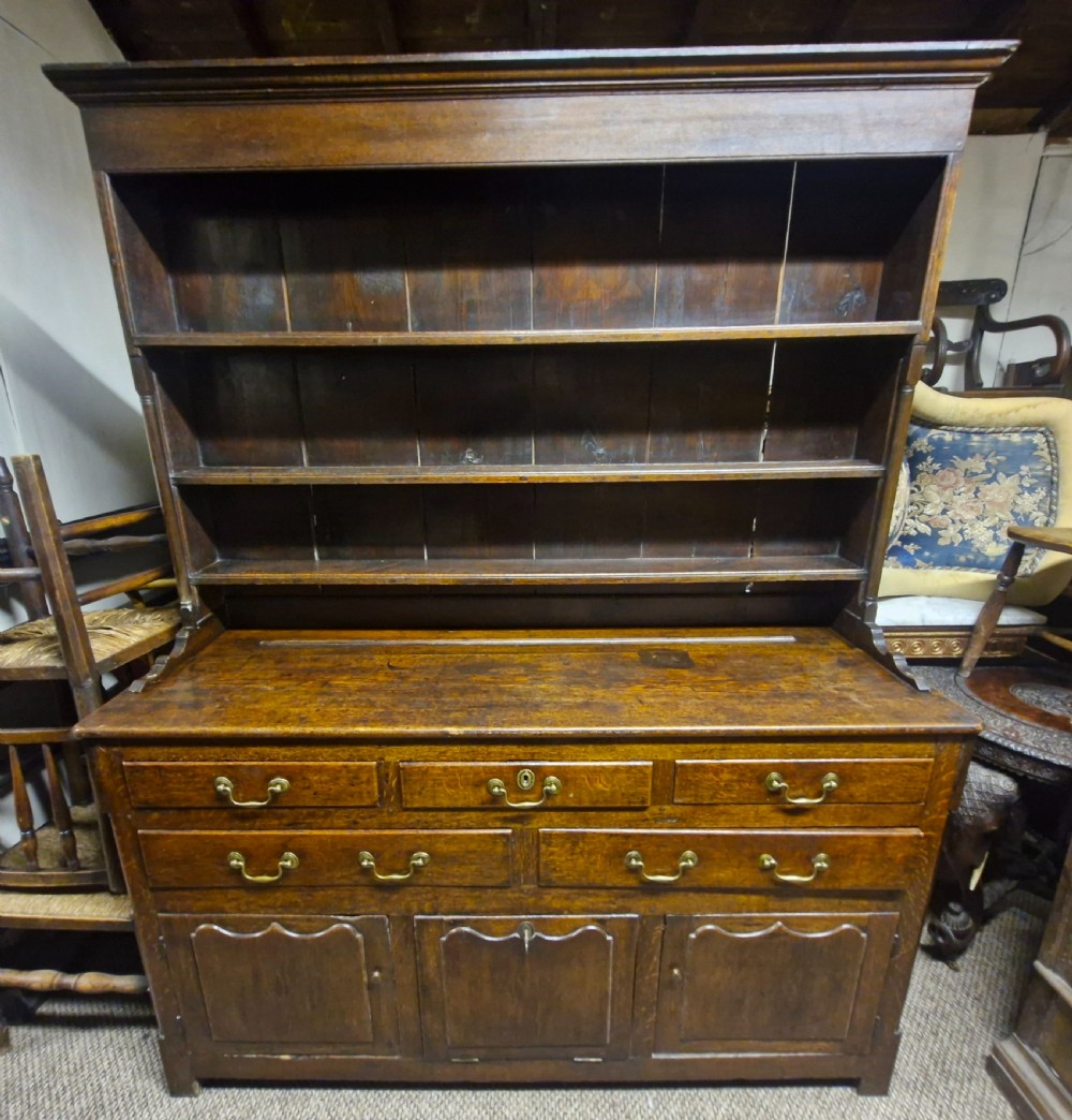 An early nineteenth-century two-part dark oak Welsh dresser featuring a three-shelf plate rack over a sideboard base with drawers and fielded panel cupboard doors. View XIX
