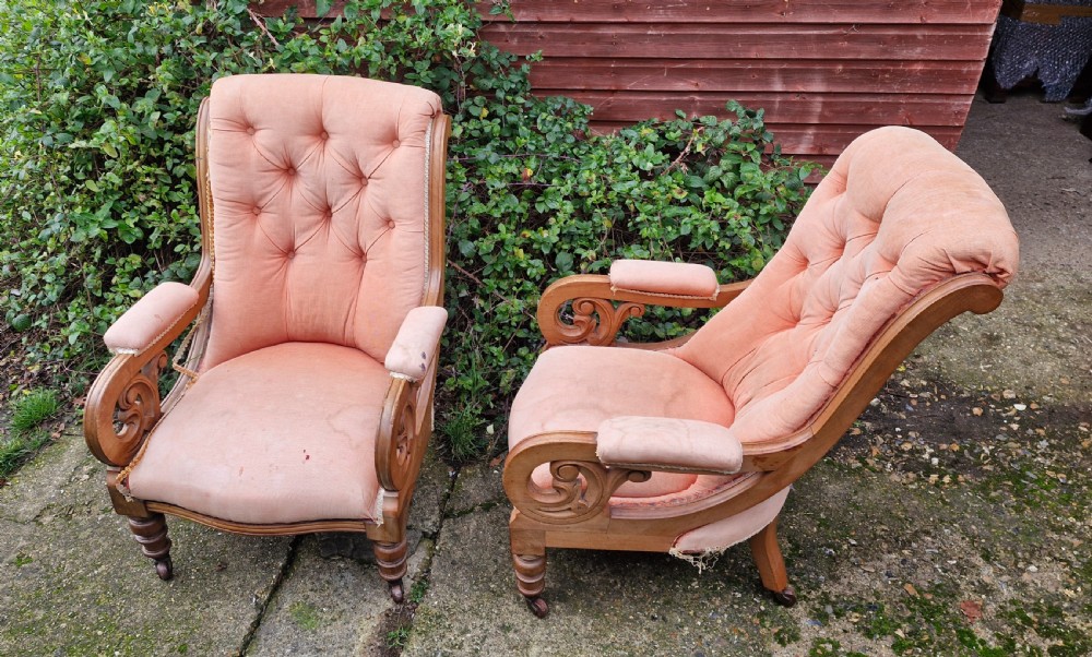 A pair of Victorian mahogany library armchairs featuring button-tufted peach fabric upholstery, scrolled wooden armrests, and turned front legs on casters.