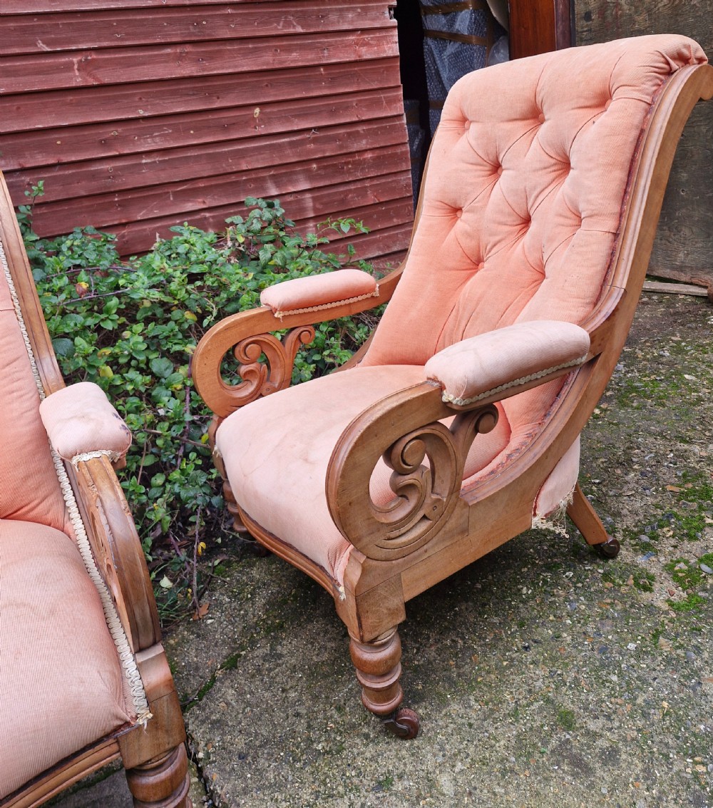 A pair of Victorian mahogany library armchairs featuring button-tufted peach fabric upholstery, scrolled wooden armrests, and turned front legs on casters. View VI