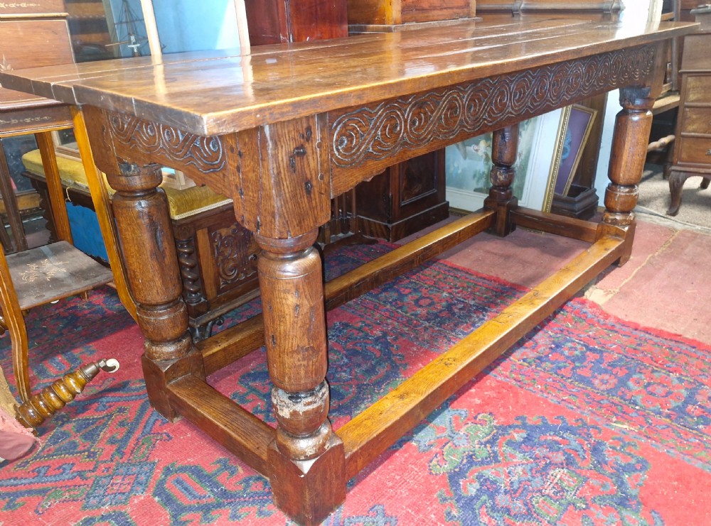 A rectangular dark oak refectory-style serving table featuring a carved frieze apron, turned legs, and a low box stretcher.