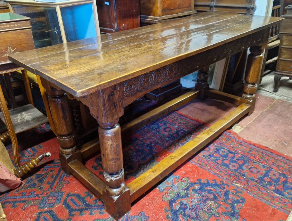 A rectangular dark oak refectory-style serving table featuring a carved frieze apron, turned legs, and a low box stretcher. View II