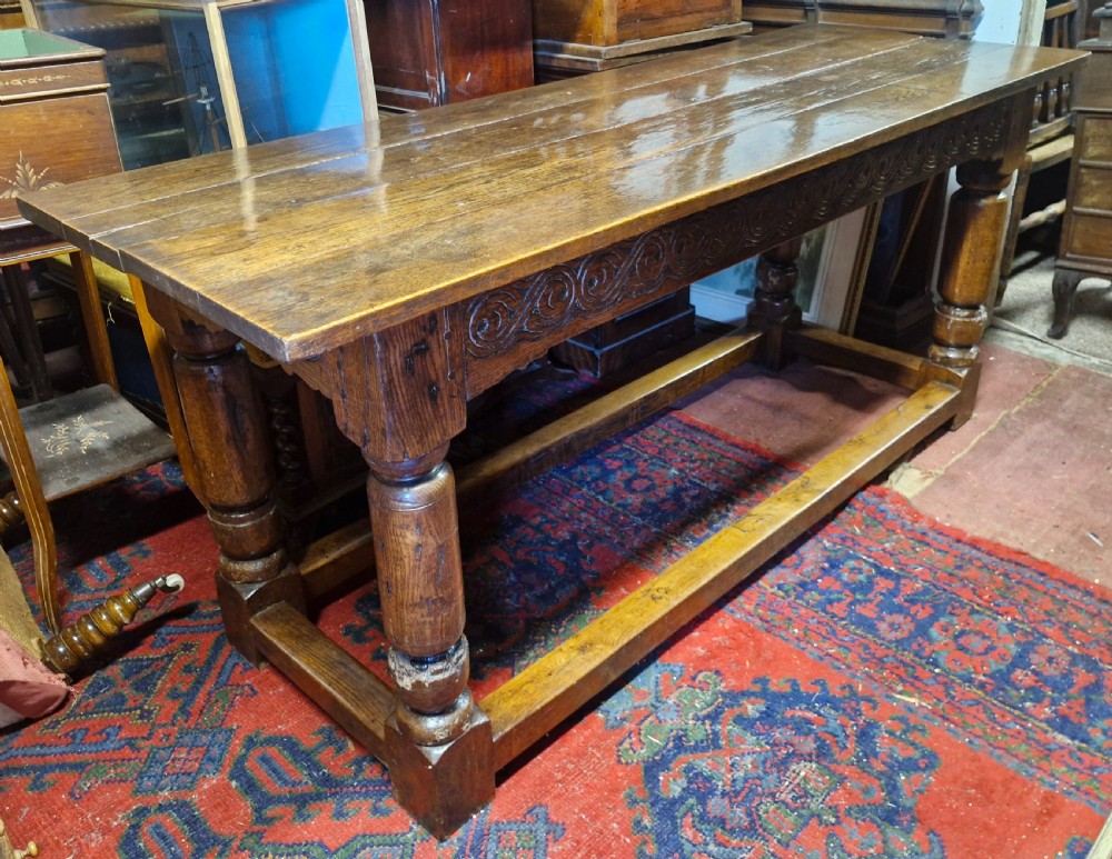A rectangular dark oak refectory-style serving table featuring a carved frieze apron, turned legs, and a low box stretcher. View III
