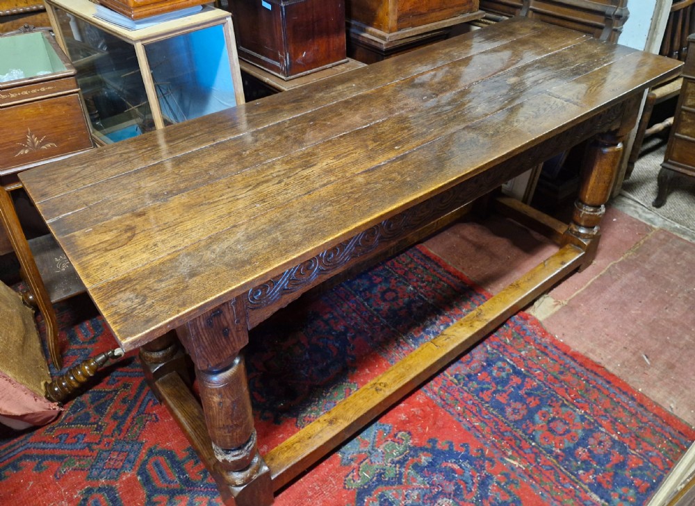 A rectangular dark oak refectory-style serving table featuring a carved frieze apron, turned legs, and a low box stretcher. View V