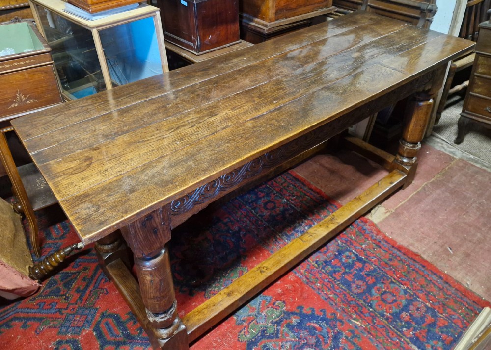 A rectangular dark oak refectory-style serving table featuring a carved frieze apron, turned legs, and a low box stretcher. View VI