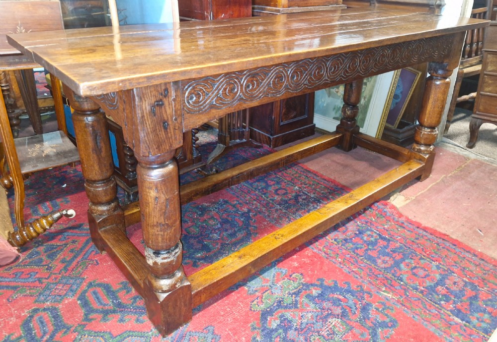 A rectangular dark oak refectory-style serving table featuring a carved frieze apron, turned legs, and a low box stretcher. View VII