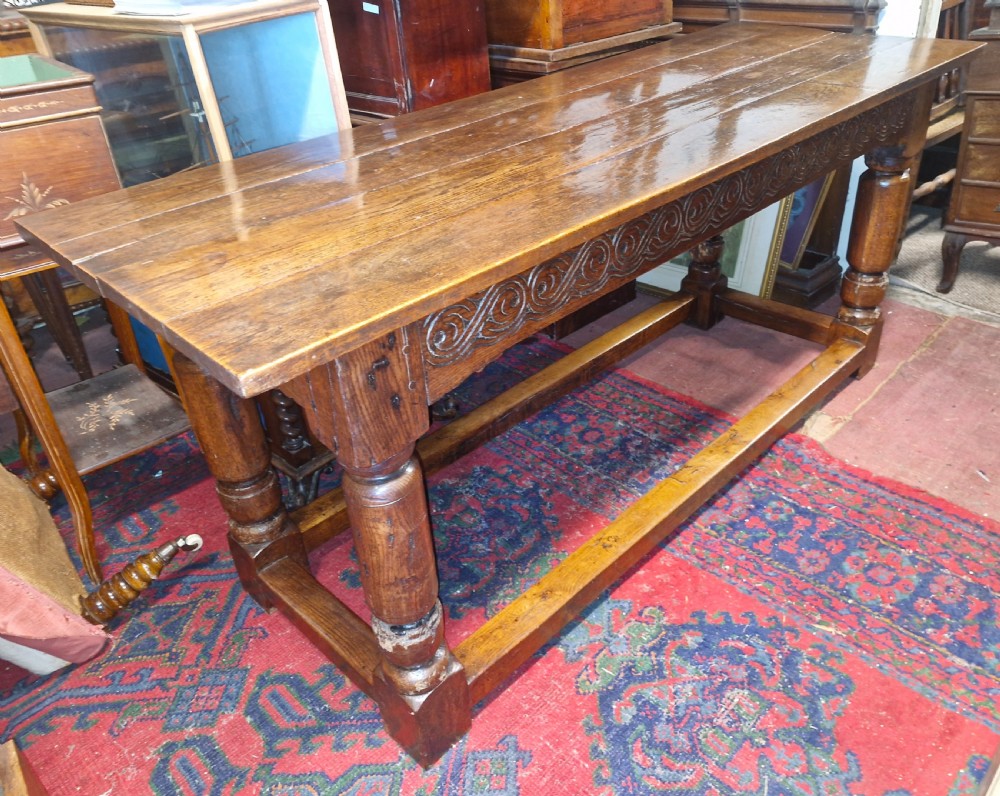 A rectangular dark oak refectory-style serving table featuring a carved frieze apron, turned legs, and a low box stretcher. View IX