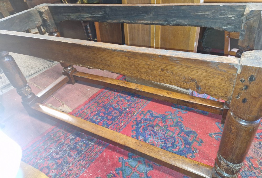 A rectangular dark oak refectory-style serving table featuring a carved frieze apron, turned legs, and a low box stretcher. View XV