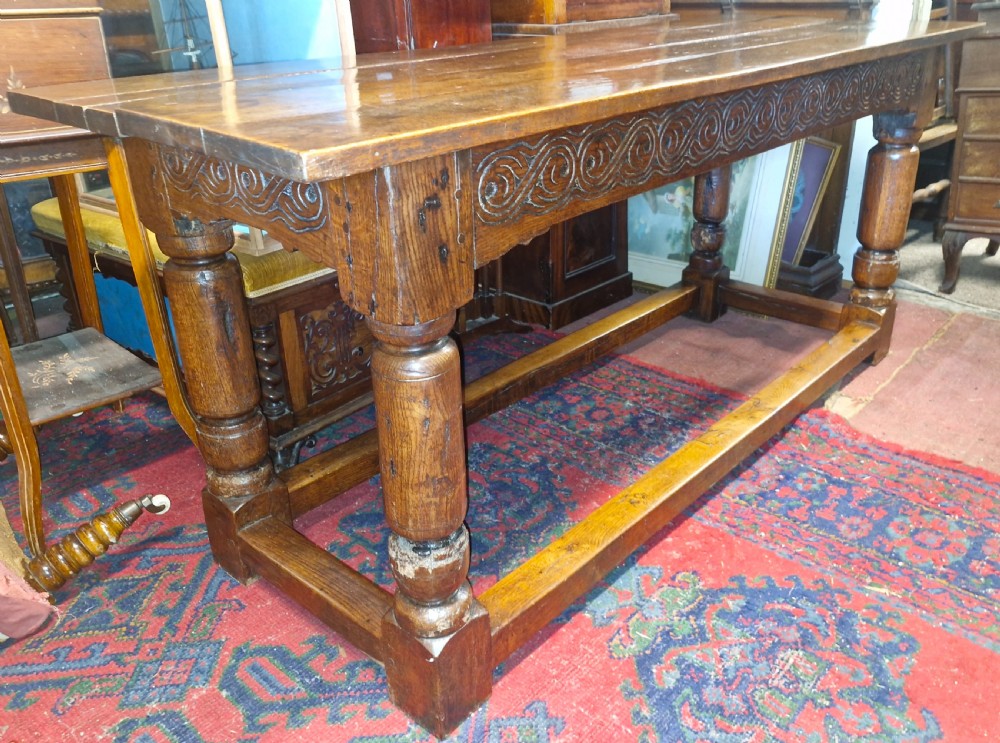 A rectangular dark oak refectory-style serving table featuring a carved frieze apron, turned legs, and a low box stretcher. View XIX