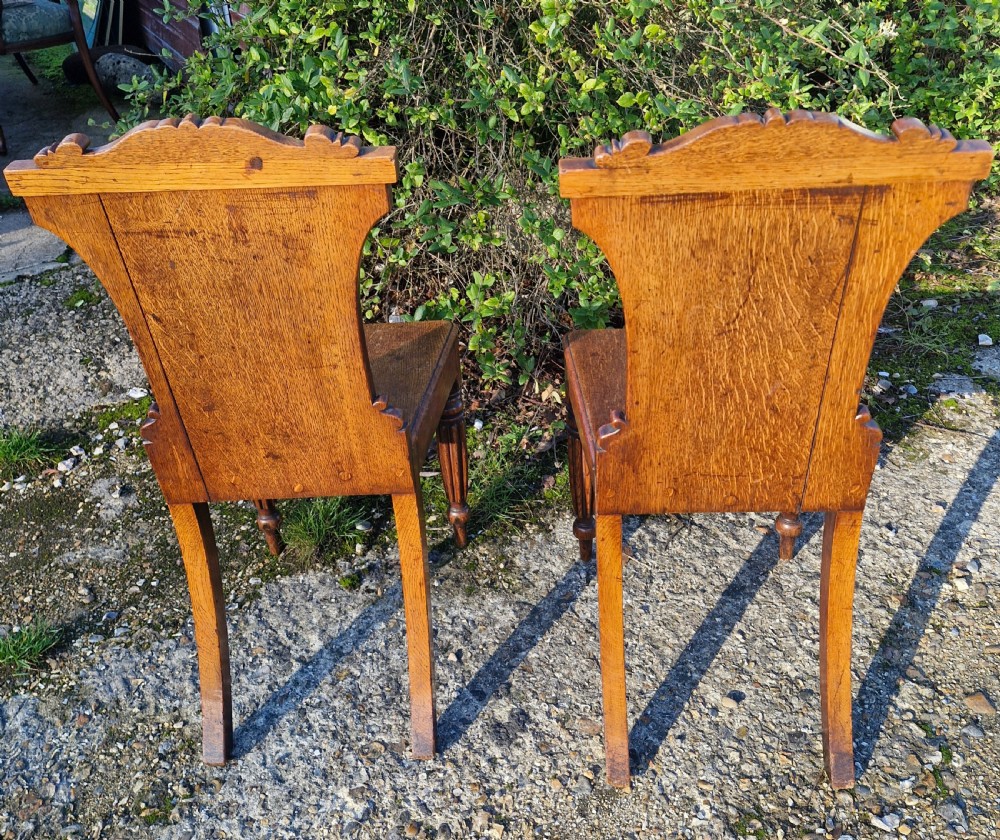 A pair of Regency oak hall chairs featuring carved scroll cresting, central shield back panels, flat wooden seats, and turned reeded front legs. View II