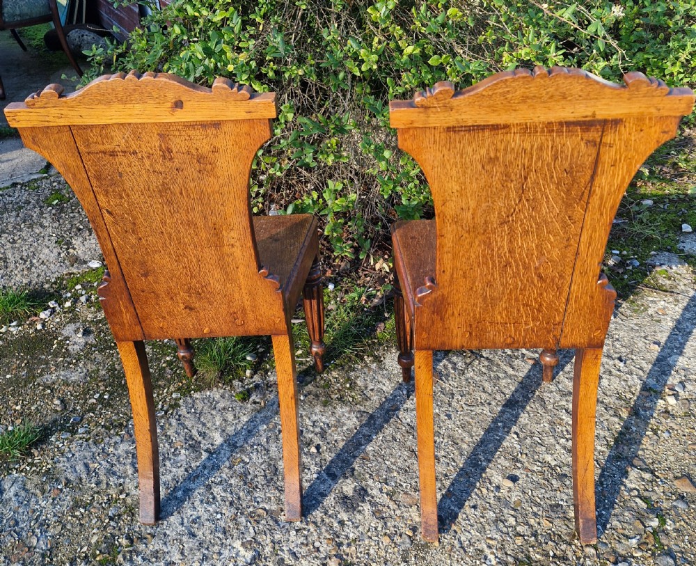 A pair of Regency oak hall chairs featuring carved scroll cresting, central shield back panels, flat wooden seats, and turned reeded front legs. View III
