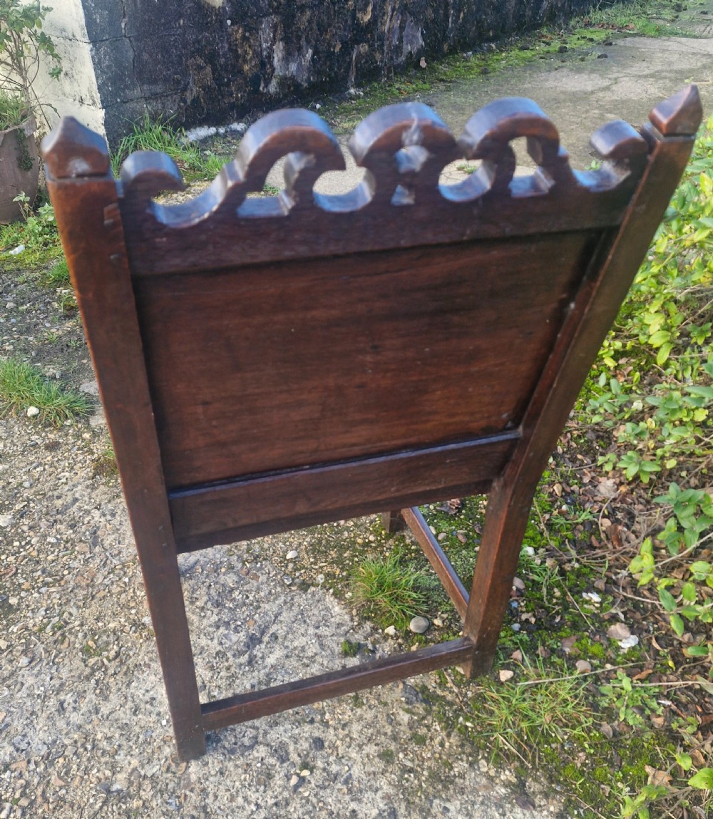 An early 18th-century dark oak wainscot armchair featuring a pierced carved cresting rail, four recessed geometric back panels, curved armrests, and turned front legs. View II