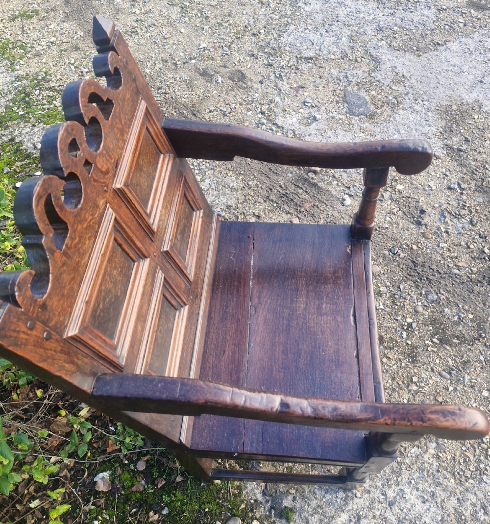 An early 18th-century dark oak wainscot armchair featuring a pierced carved cresting rail, four recessed geometric back panels, curved armrests, and turned front legs. View VII