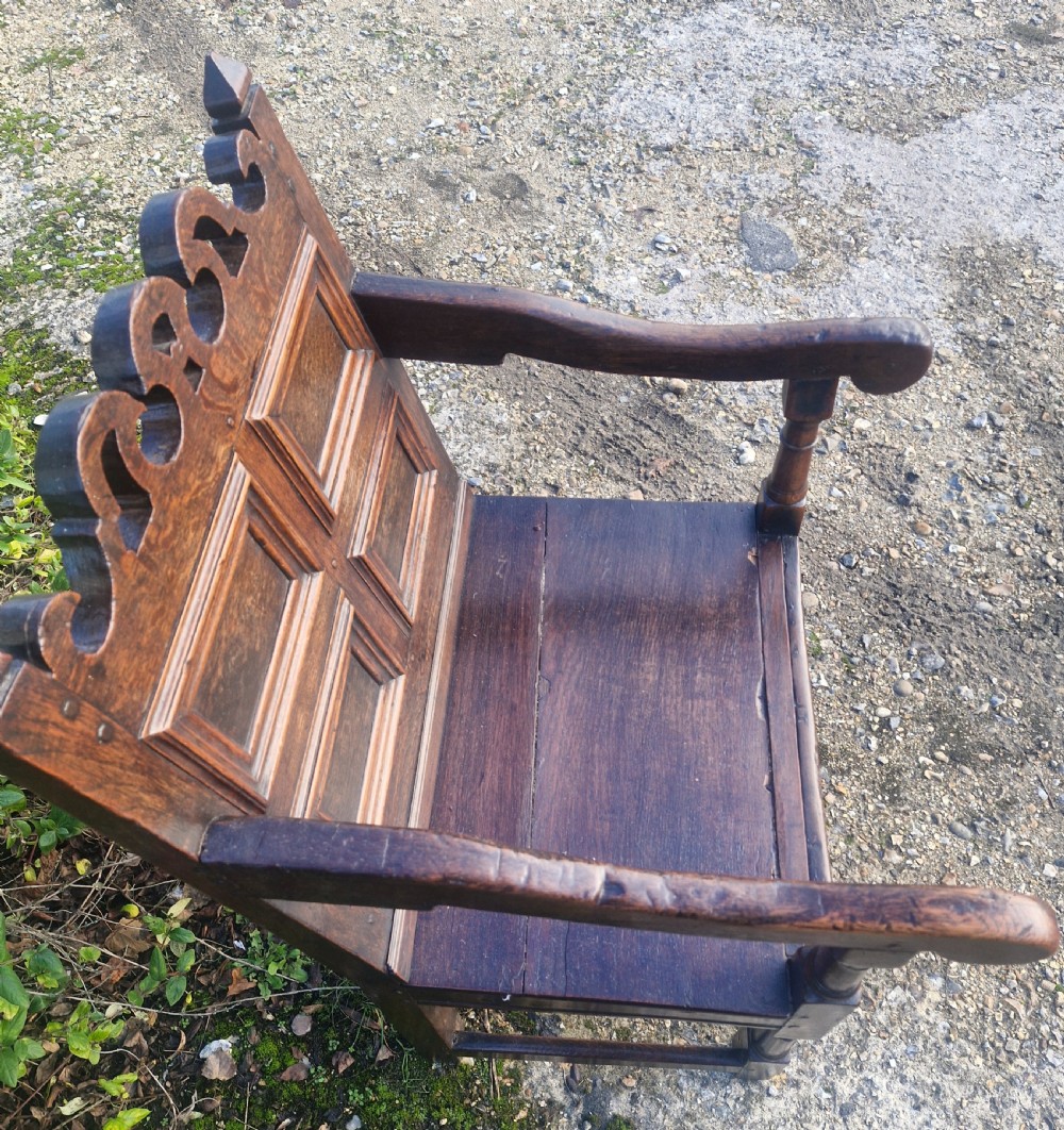 An early 18th-century dark oak wainscot armchair featuring a pierced carved cresting rail, four recessed geometric back panels, curved armrests, and turned front legs. View VIII