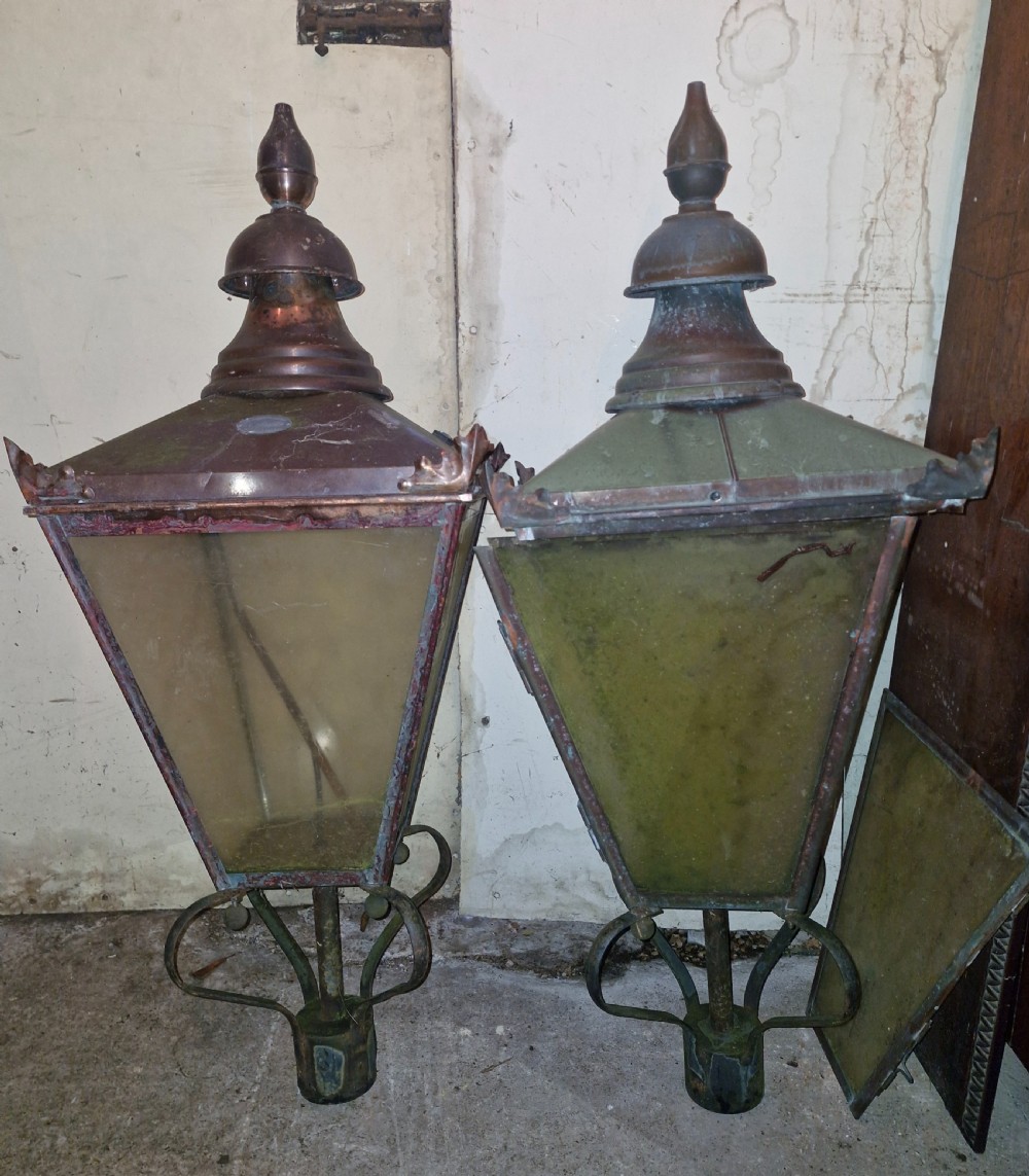 A pair of antique copper street lantern tops featuring tapered glazed panels, decorative finials, and scrolled iron mounts.