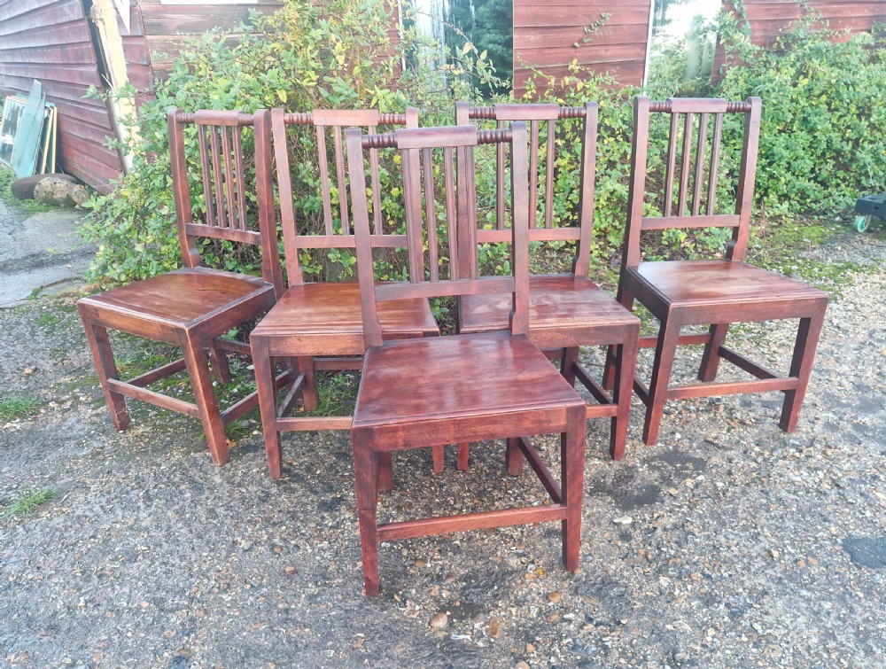 A set of five early Victorian dark-stained timber dining chairs featuring vertical slat backs, turned top rails, solid wooden seats, and straight legs with stretchers.