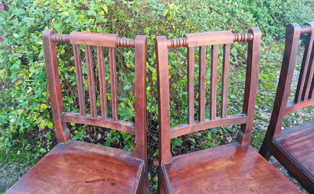 A set of five early Victorian dark-stained timber dining chairs featuring vertical slat backs, turned top rails, solid wooden seats, and straight legs with stretchers. View II