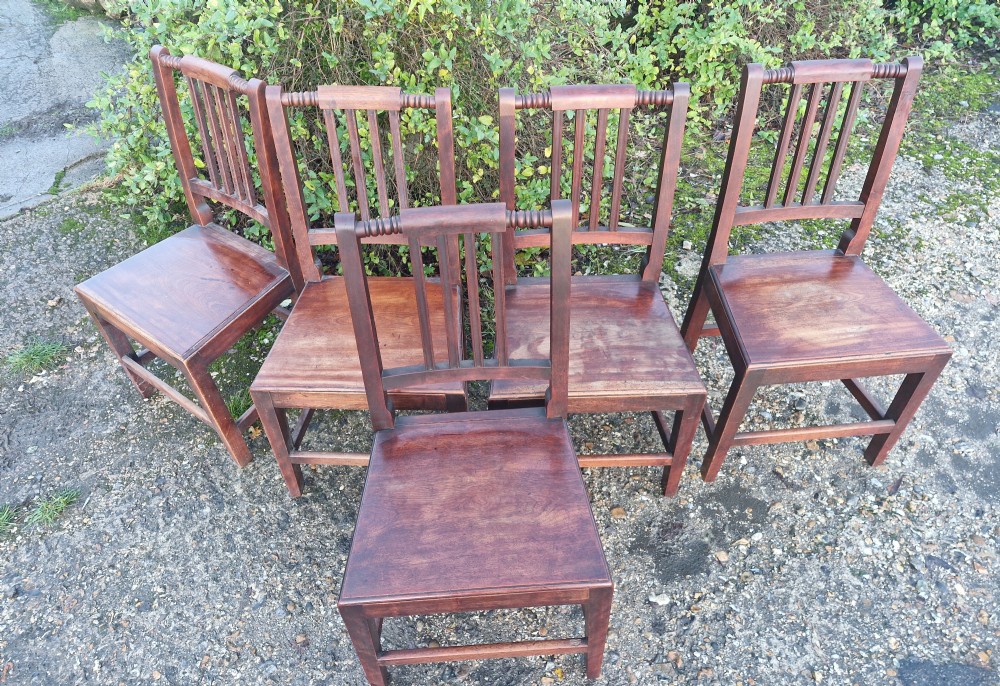 A set of five early Victorian dark-stained timber dining chairs featuring vertical slat backs, turned top rails, solid wooden seats, and straight legs with stretchers. View IV