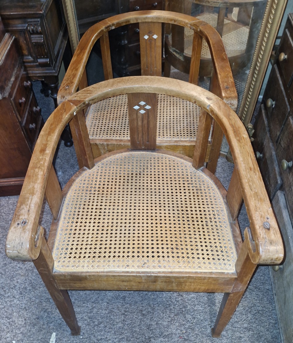 A pair of Anglo Indian Art Deco teak armchairs featuring curved horseshoe backrests with diamond inlay and woven cane seats.